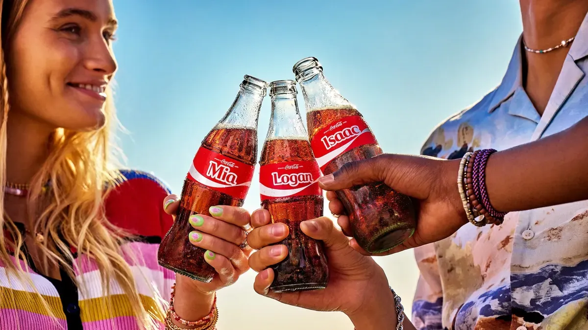 Three people cheers with Coke bottles emblazoned with names as part of the brand&#x27;s &#x27;Share a Coke&#x27; campaign.